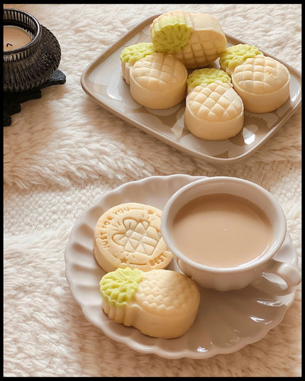 Ein Leinwandbild von einer Tasse Kaffee und Ananas-geformten Keksen auf einem Teller, arrangiert auf einem weichen, flauschigen Untergrund.