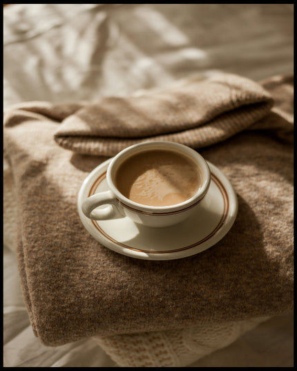 Ein Leinwandbild von einer Tasse Kaffee auf einem gemütlichen, beigen Pullover.