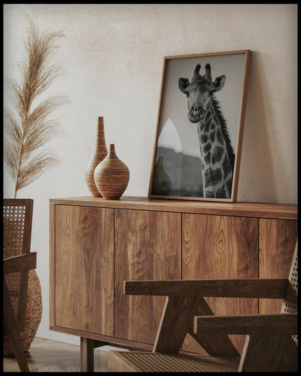 Ein gerahmtes Poster vom Kopf einer Giraffe in schwarz-weiß, auf einer Holzkommode an die Wand angelehnt