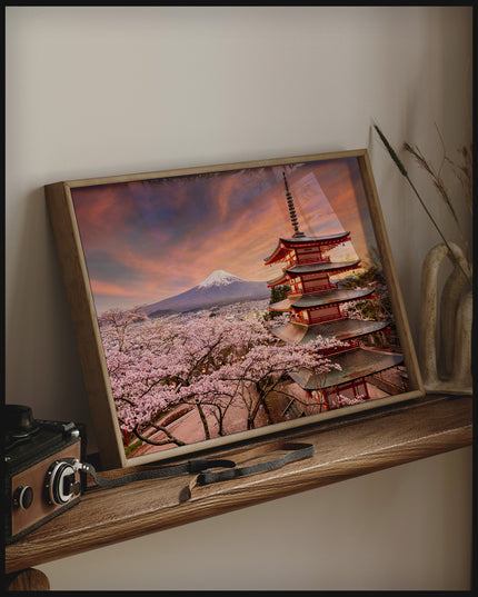 Ein gerahmtes Poster von der Chureito-Pagode vor dem Fuji-Berg bei Sonnenuntergang, umgeben von Kirschblüten, auf einem Holzregal an die Wand angelehnt