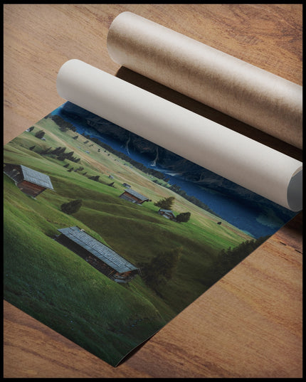 Ein Poster von einer grünen Alm mit kleinen Hütten und den Dolomiten im Hintergrund, gerollt auf einer Holzoberfläche liegend