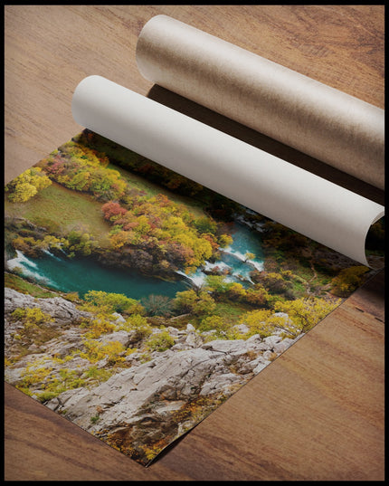 Ein Poster von einem Fluss der sich, umgeben von mehreren Büschen, durch eine Berglandschaft erstreckt, gerollt auf einer Holzoberfläche liegend