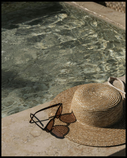 Ein Poster von einem Sonnenhut und einer Sonnenbrille neben einem Swimming Pool aus Marmor.