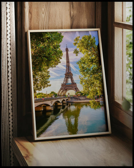 Ein gerahmtes Poster vom Eiffelturm der sich im Wasser spiegelt, vor einem Fenster an die Wand angelehnt