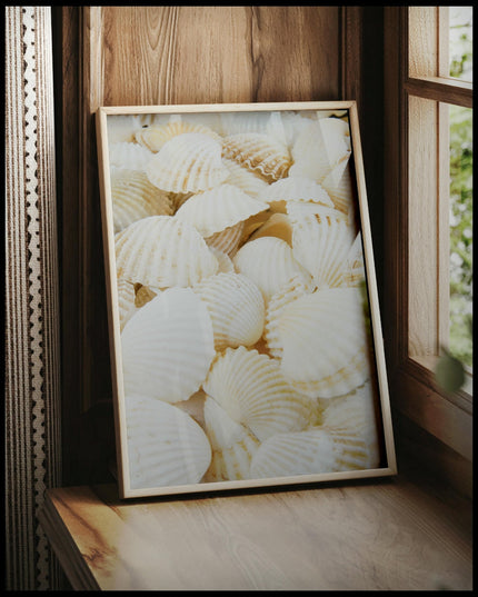 Ein gerahmtes Poster von weißen Muscheln, vor einem Fenster an die Wand angelehnt